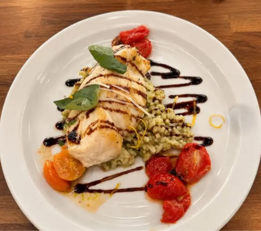 A plated entrée over green risotto with roasted tomatoes and balsamic